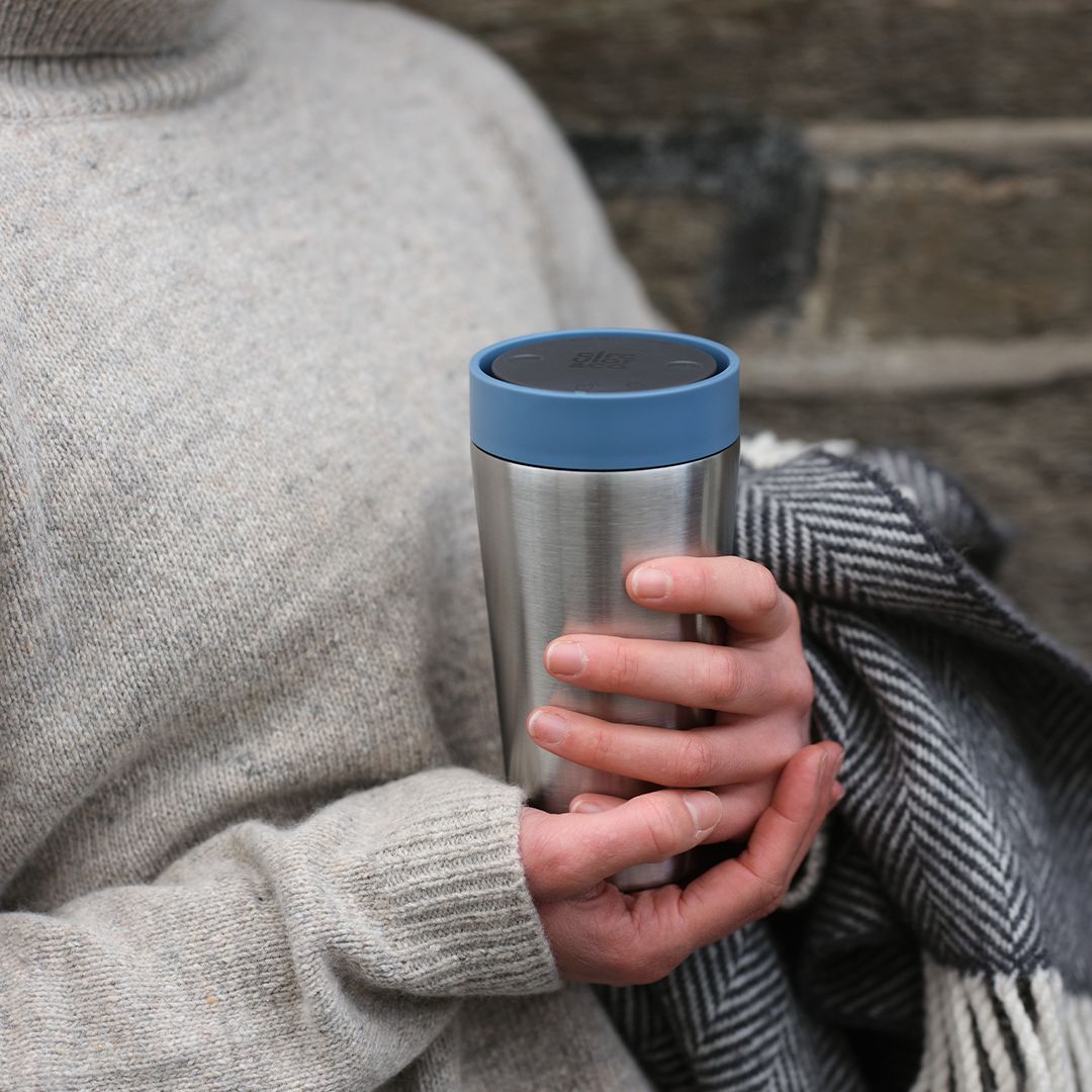 steel reusable cup on its side next to glasses and newspaper